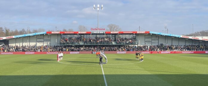 Die Spieler der Mannschaften SC Verl und Dynamo Dresden stehen am Mittelkreis wärhend der Schweigeminute für den Spieler Agi Diawusie des Jahn Regensburg, welcher Anfang der Woche unerwartet verstarb.